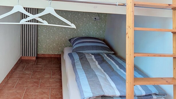 A small, compact room with a bed, a wooden ladder, and a clothing rack. - Das Dorfnest by Interhome (Wanna)