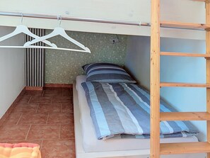 Quarto pequeno e compacto com uma cama, uma escada de madeira e um cabideiro.