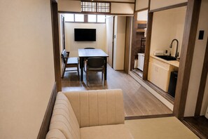 A modern interior with a sofa, a dining table with chairs, a kitchen area, and a television mounted on the wall. - Kyo-ikkenmachiya Satoi Itoyufu (Kyoto)