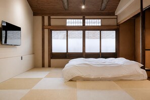 A room with tatami flooring, a bed, a television on the wall, and a large window with a view. - Kyo-ikkenmachiya Satoi Itoyufu (Kyoto)