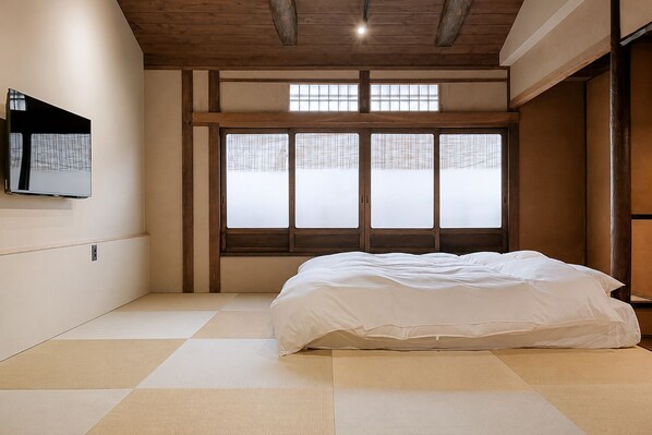 A room with tatami flooring, a bed, a television on the wall, and a large window with a view. - Kyo-ikkenmachiya Satoi Itoyufu (Kyoto)