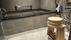 A modern bathroom with a bathtub, a wooden stool, and a shower area. - Kyo-ikkenmachiya Satoi Itoyufu (Kyoto)