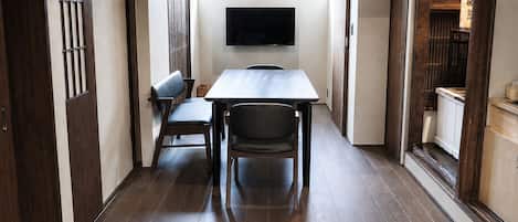 Un couloir étroit avec une table et des chaises, un téléviseur fixé au mur et des meubles de rangement en bois.