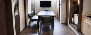 A narrow hallway with a dining table and chairs, a television mounted on the wall, and wooden cabinets. - Kyo-ikkenmachiya Satoi Itoyufu (Kyoto)