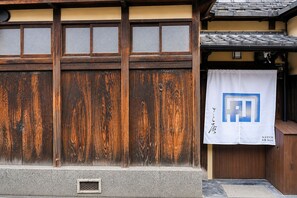 A traditional Japanese building with wooden sliding doors and a white banner with a logo. - Kyo-ikkenmachiya Satoi Itoyufu (Kyoto)