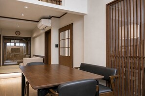 Ein modernes Interieur mit einem Holzesstisch, schwarzen Stühlen, einer Schiebetür mit vertikalen Jalousien und einer Decken-Klimaanlage.