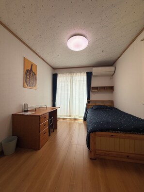 Une chambre à coucher avec un lit en bois, un bureau avec des tiroirs, une chaise, un radiateur et une fenêtre avec des rideaux.