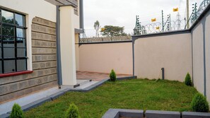 A residential area with a paved courtyard, a small lawn, and a building with a window and a door.