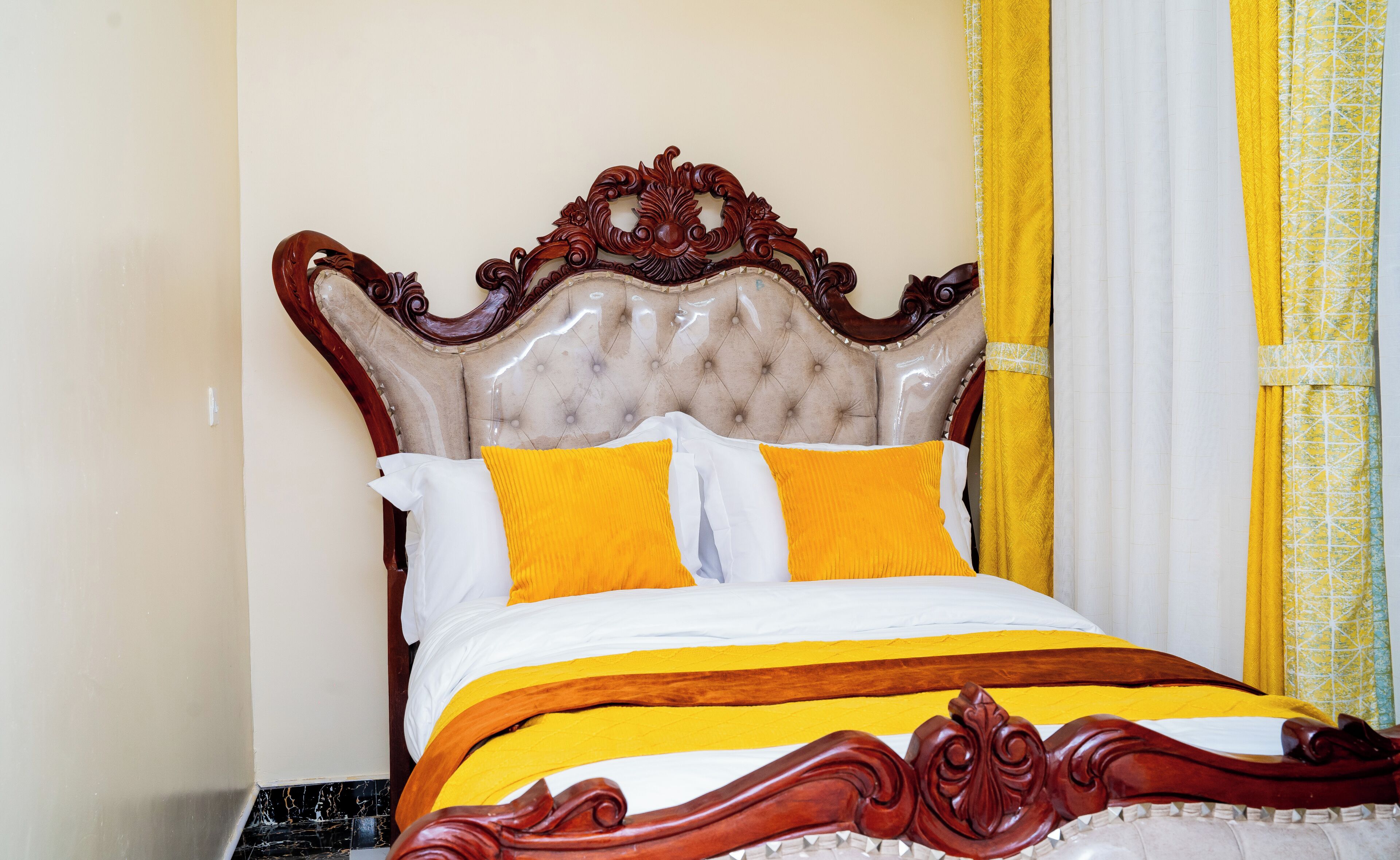 Una cama con cabecera de madera, ropa de cama blanca y amarilla, y una cortina amarilla.