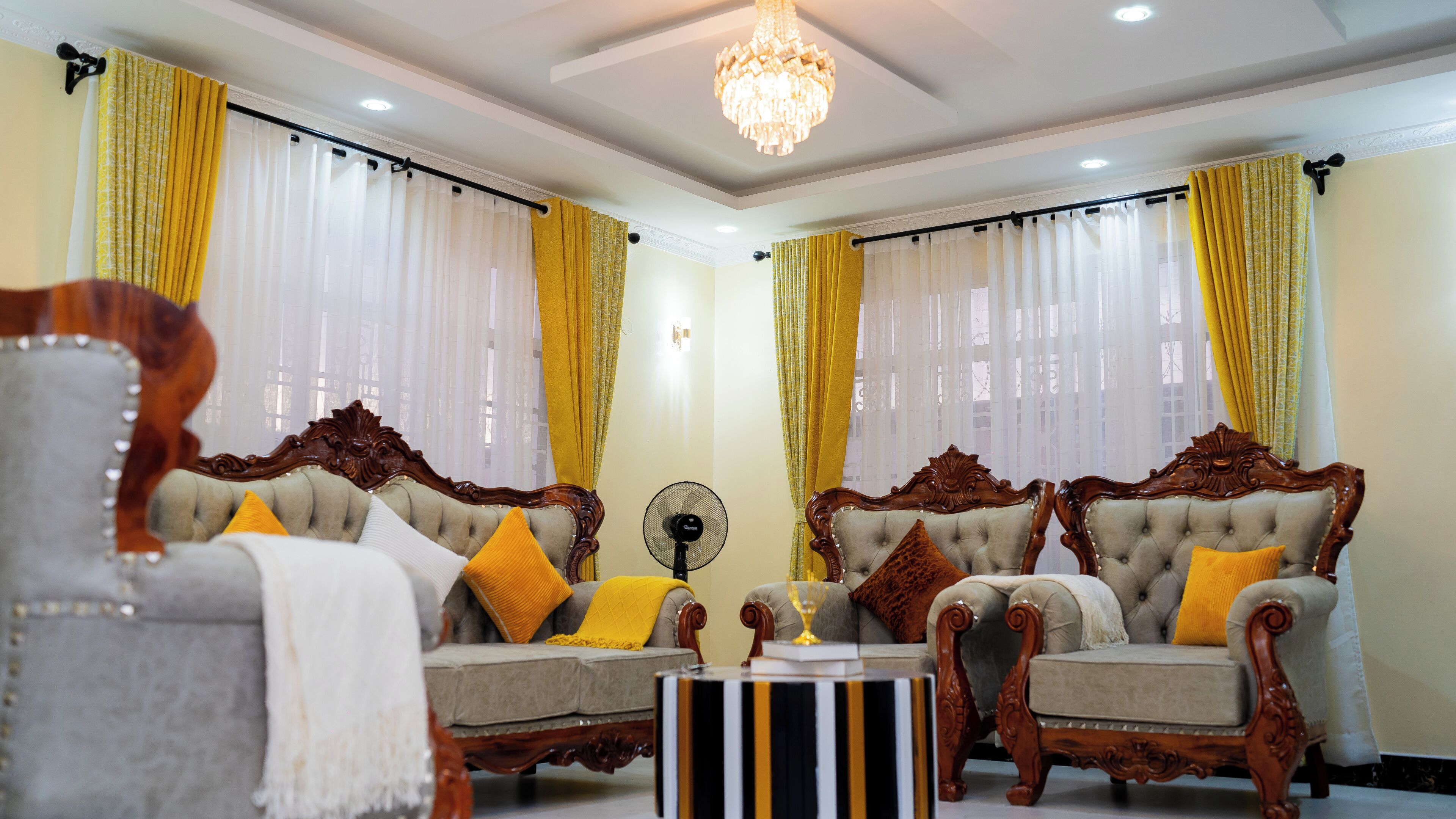 A room with two ornate sofas, a fan, and a chandelier.