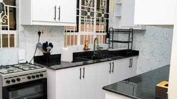 A kitchen with a gas stove, oven, black countertop, white cabinets, and a window with decorative iron bars.