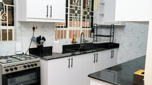 A kitchen with a gas stove, oven, black countertop, white cabinets, and a window with decorative iron bars.
