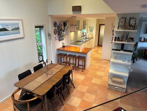 A modern kitchen with a central island, a dining area with a wooden table and chairs, and a living space with shelves and decorative items. - Kikorangi Haven - Pets Welcome (Nelson)