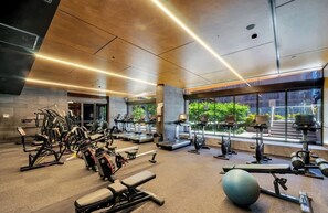A modern gym with various exercise equipment, large windows, and a view of greenery outside. - LaneStay - 2BR Southern Cross & Marvel, Pool & Gym (Melbourne)