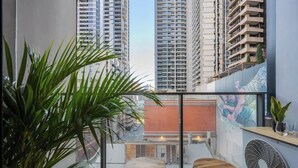 Ein Balkon mit zwei Holzstühlen, einem großen Kübelpflanzen und einem Wandventilator.