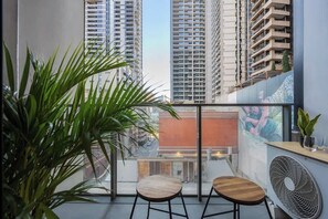 A balcony with two wooden chairs, a large potted plant, and a wall-mounted fan. - LaneStay - 2BR Southern Cross & Marvel, Pool & Gym (Melbourne)