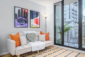 A modern living room with a white sofa, orange and white cushions, a patterned rug, and two framed artworks on the wall. - LaneStay - 2BR Southern Cross & Marvel, Pool & Gym (Melbourne)