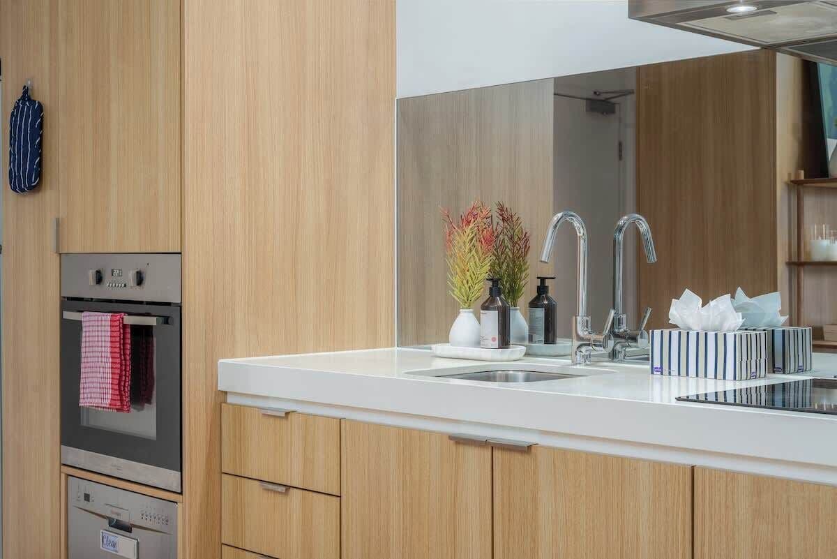 Une cuisine moderne avec des meubles en bois, un évier en acier inoxydable et un four encastré.