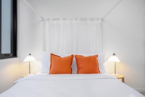A bed with white bedding and two orange pillows, flanked by two bedside lamps on wooden nightstands. - LaneStay - 2BR Southern Cross & Marvel, Pool & Gym (Melbourne)