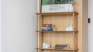 Ein Zimmer mit Glastisch, grünen Stühlen, einem hölzernen Bücherregal und einem gerahmten Bild.