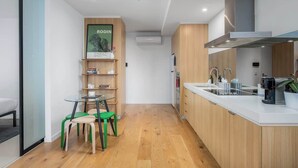 Eine moderne Küche mit weißer Arbeitsplatte, Holzschränken und einem eingebauten Herd. Es gibt eine kleine Essecke mit einem Glastisch und grünen Stühlen.