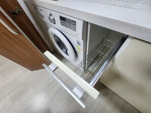 Eine Waschmaschine mit Frontöffnung, einem Bedienfeld, einem Metallgestell und einer Holztür.