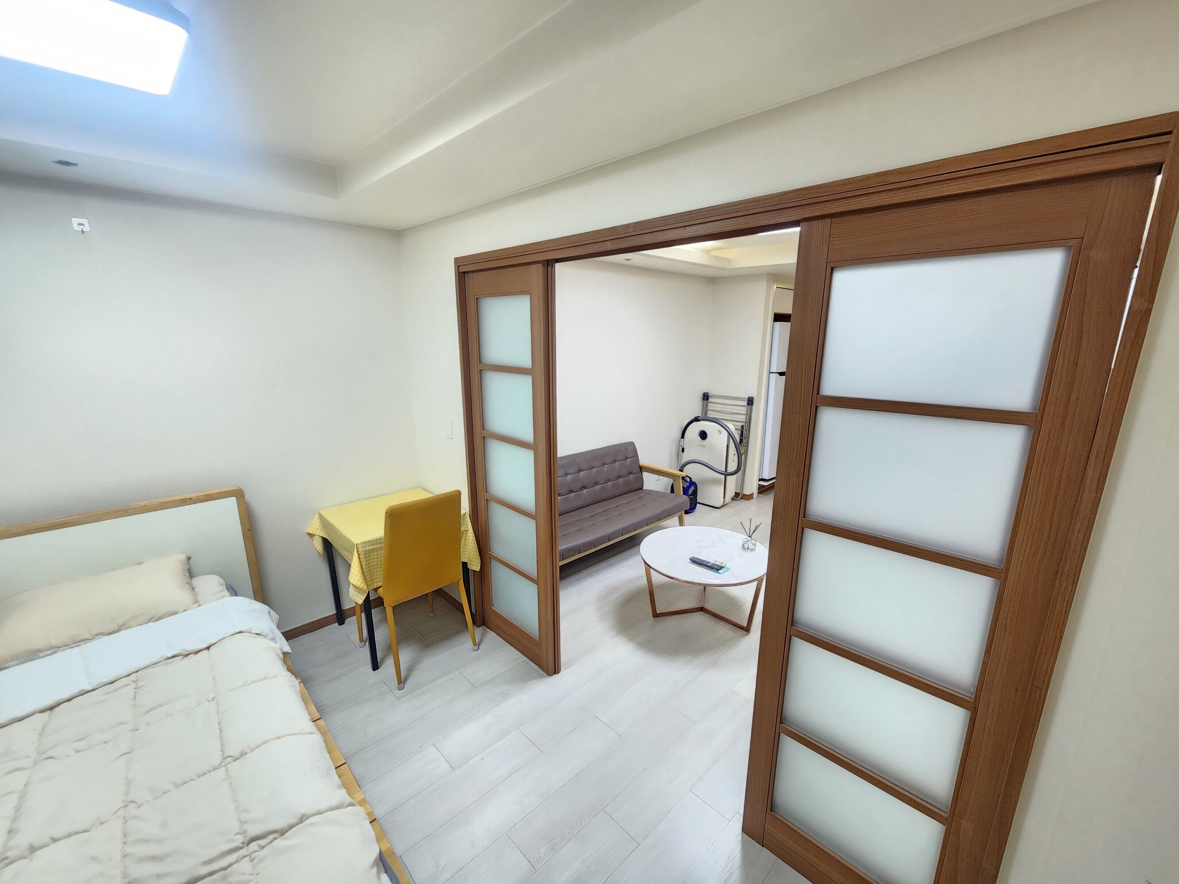 A room with a bed, a yellow table, a gray sofa, a white coffee table, and a sliding door with frosted glass panels.