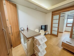 Habitación pequeña con kitchenette, televisión, un mueble de madera y puerta corredera que da a un balcón.