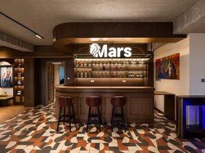Zona de bar con un letrero 'Mars', taburetes y suelo estampado.
