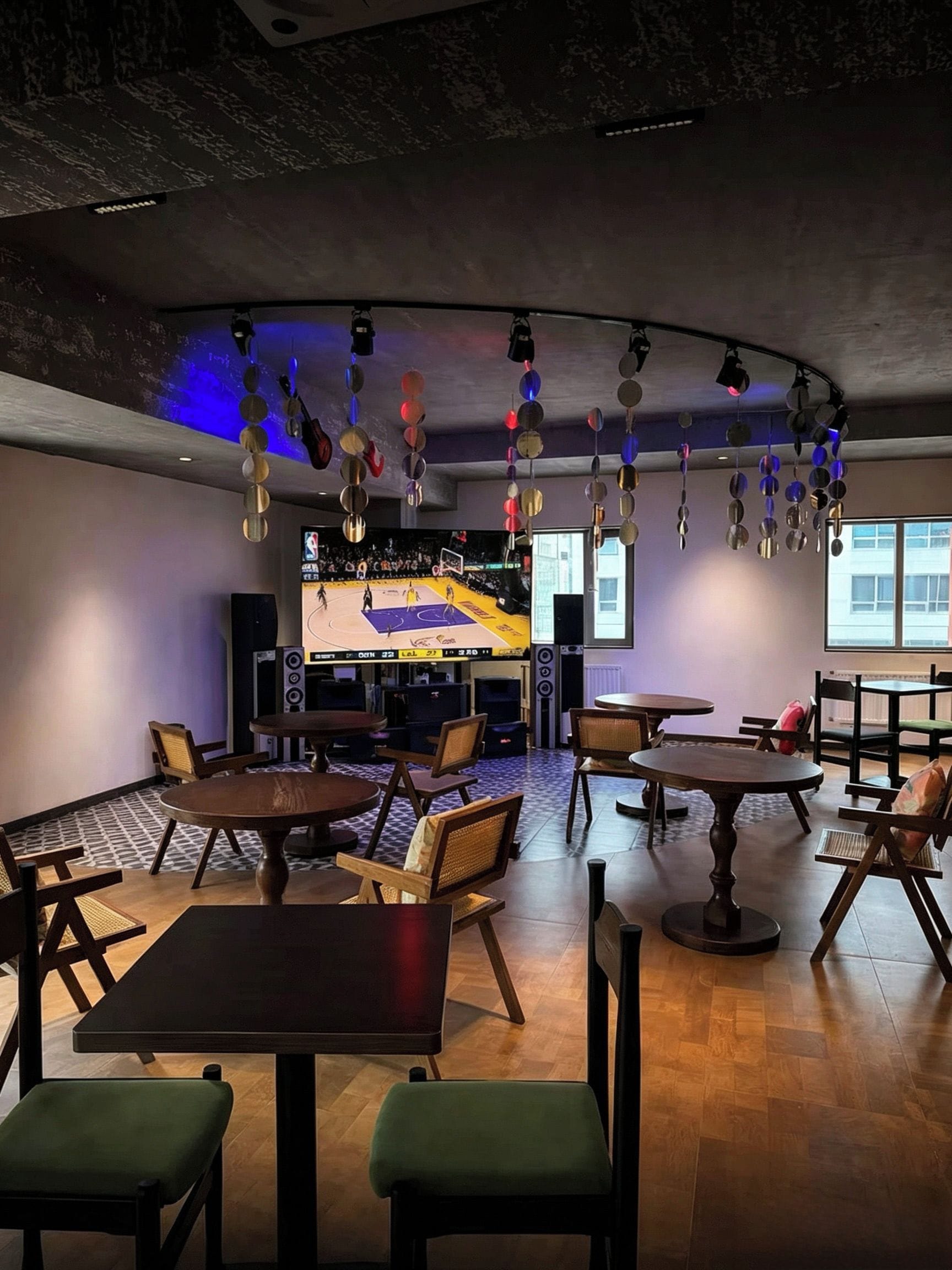 Amplio espacio interior con diversas disposiciones de asientos, incluyendo mesas y sillas, y una pantalla grande mostrando un partido de baloncesto.
