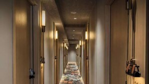 Un pasillo de hotel con piso alfombrado, puertas a ambos lados y lámparas fijadas en la pared.