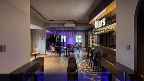 Una zona de bar con barra y taburetes, un área de estar con mesas y sillas, y un suelo con diseño.