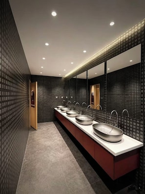 Un baño moderno con un tocador amplio, varios lavamanos y un espejo grande.