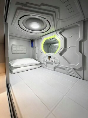 Una habitación futurista con una cama litera, un panel de control y un espejo hexagonal.
