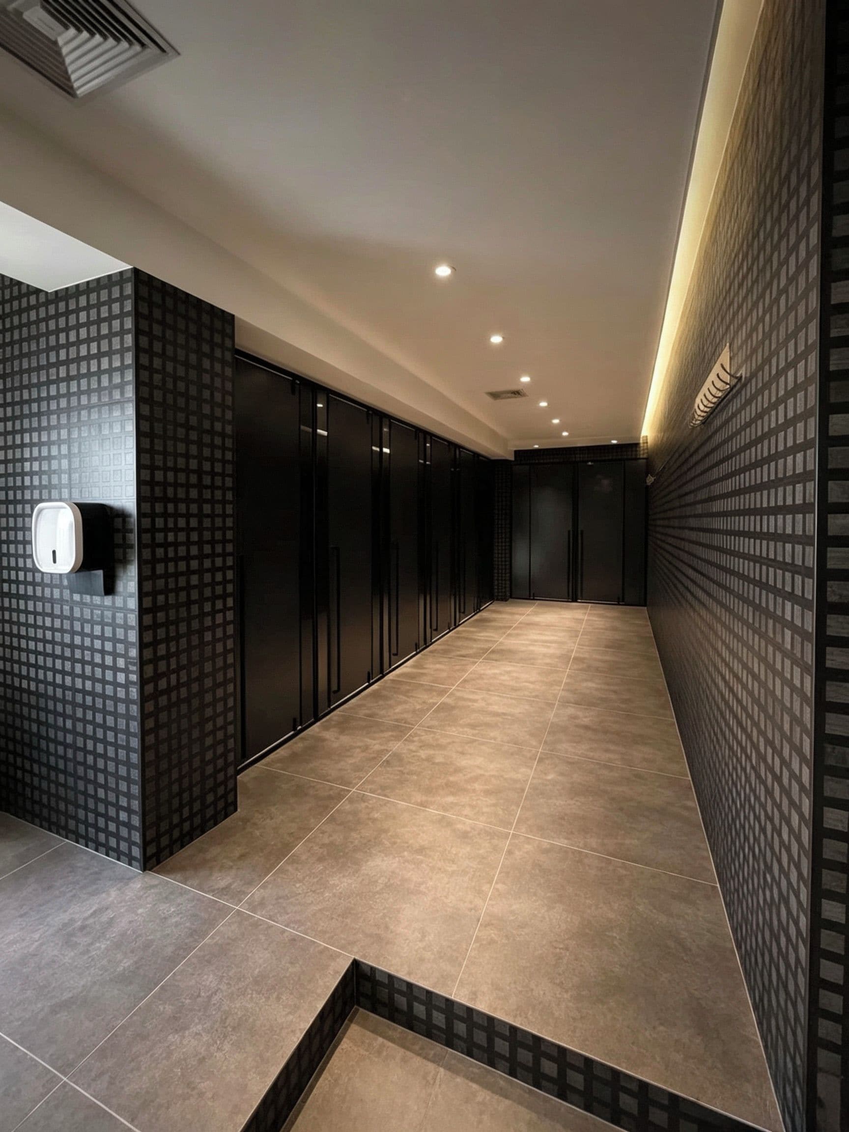 A hallway with a patterned wall, a hand sanitizer dispenser, and a tiled floor.
