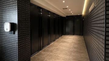 A hallway with a patterned wall, a hand sanitizer dispenser, and a tiled floor.