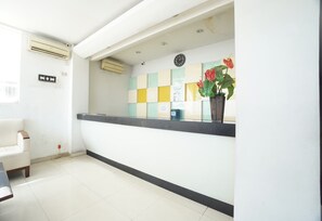 A reception area with a reception desk, a clock, a potted plant, and a wall-mounted air conditioning unit.