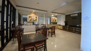 Un espace repas moderne avec une table et des chaises au centre, un coin cuisine équipé d’un réfrigérateur et d’une cuisinière, et des œuvres d’art accrochées aux murs.