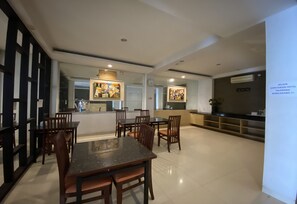 A modern dining area with a central table and chairs, a kitchen area with a refrigerator and stove, and artwork on the walls.