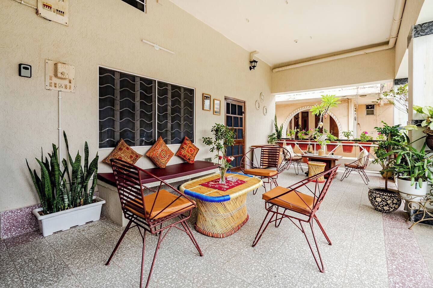 An outdoor seating area with wicker furniture, a sofa, and a coffee table. There are potted plants and a view of the street in the background.
