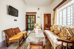 A room with a wooden sofa, a wooden table, and a television mounted on the wall.