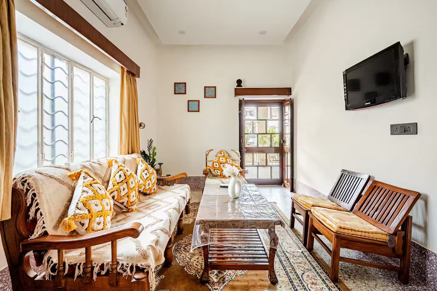 Een woonkamer met een bank, fauteuils, een salontafel en een aan de muur bevestigde televisie.
