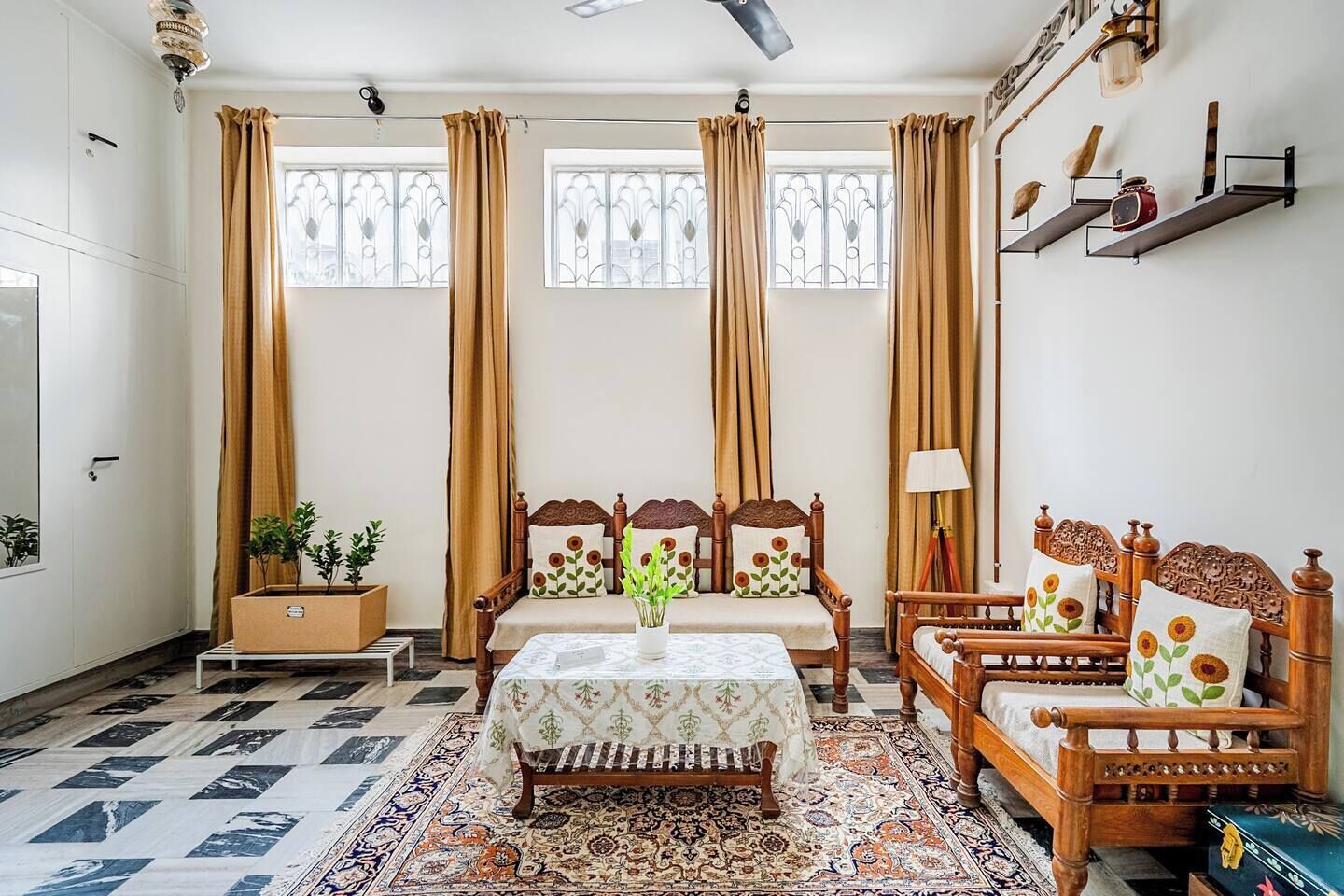 A room with a wooden bed, a wooden chair, a table with a tablecloth, and a patterned rug.
