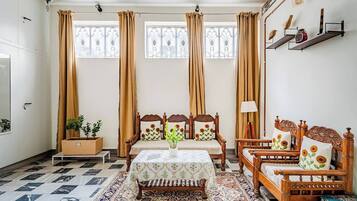 A room with a wooden bed, a wooden chair, a table with a tablecloth, and a patterned rug.