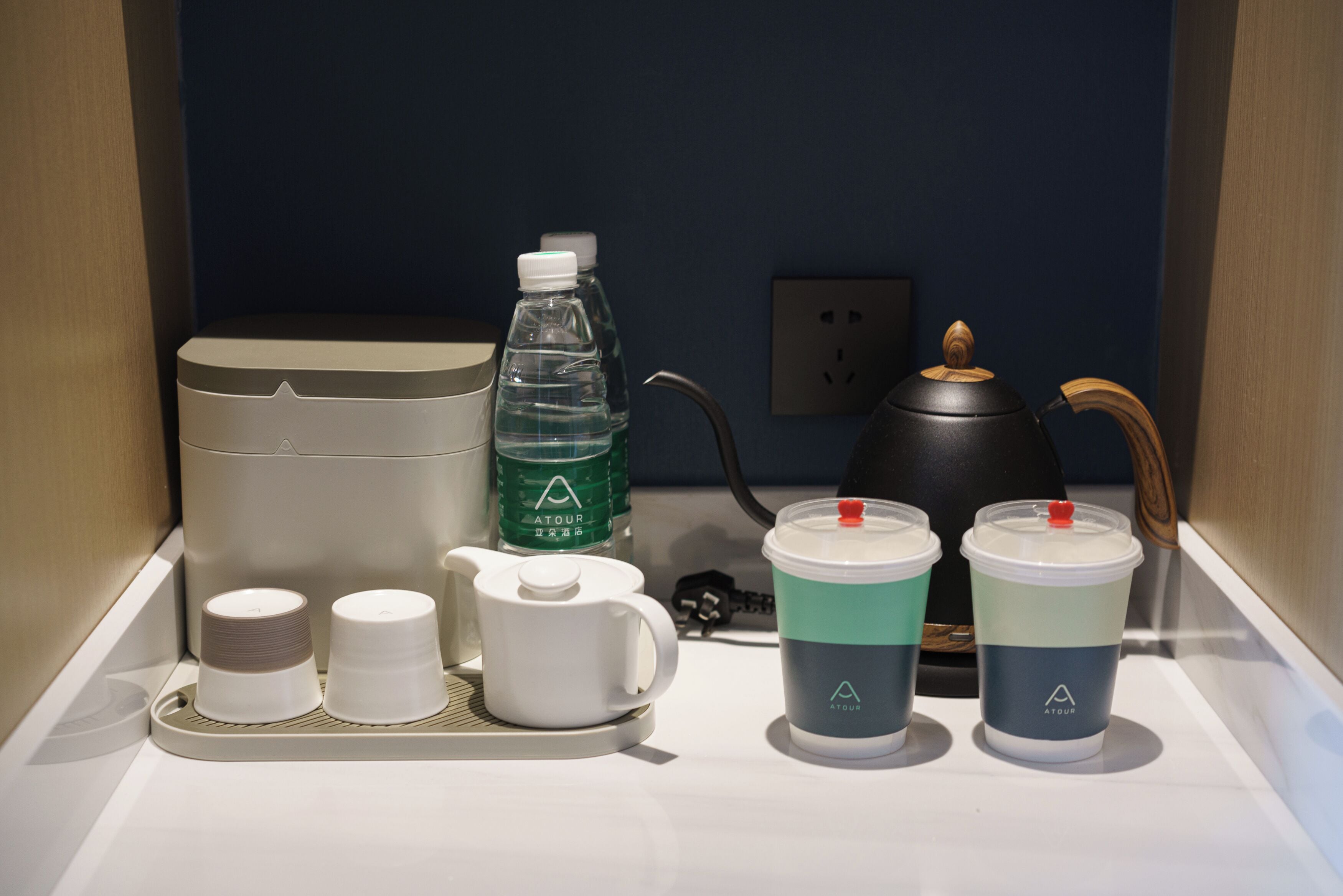 Una kitchenette con cafetera, botella de agua, tetera y dos tazas sobre una bandeja.