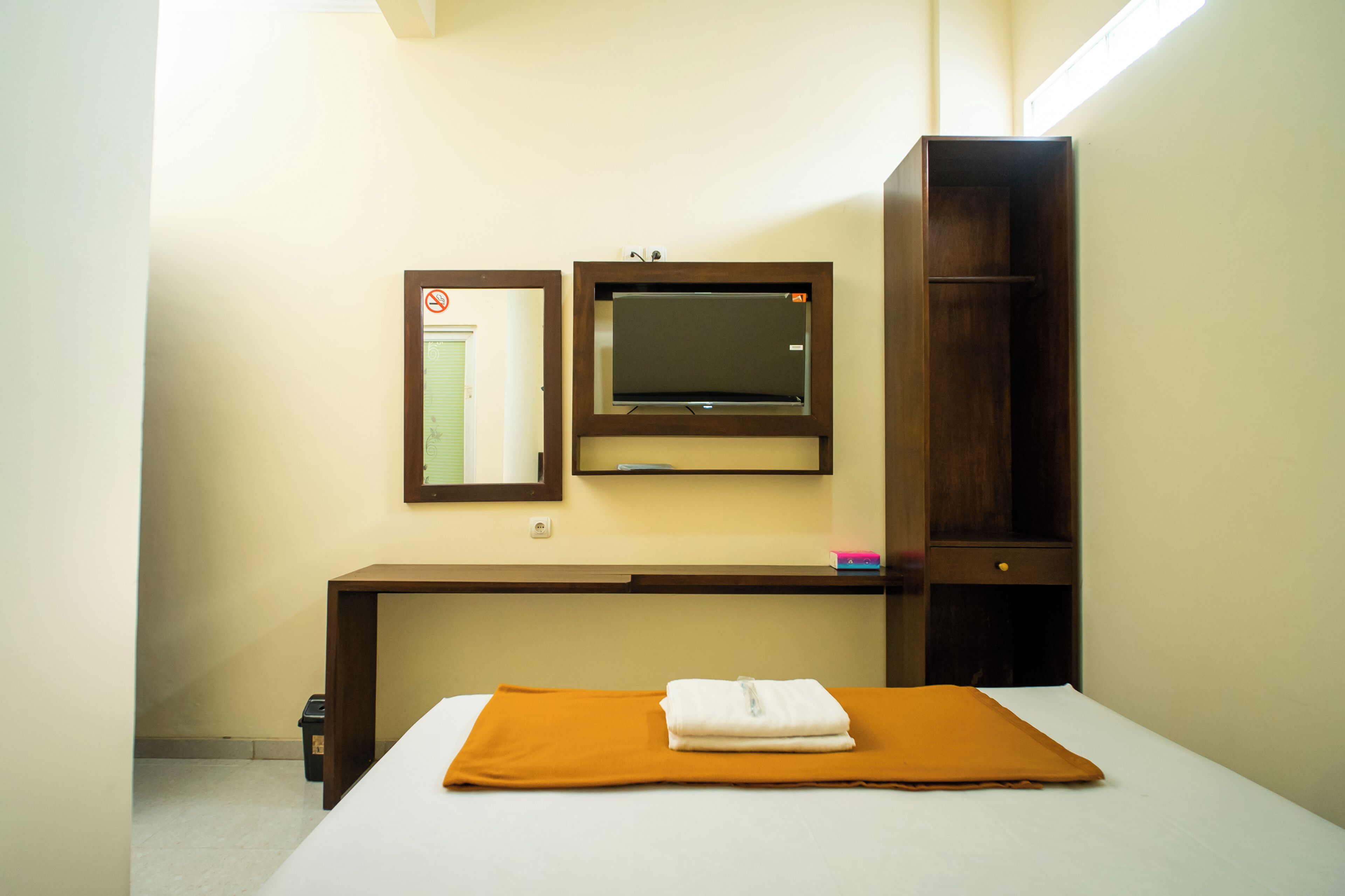 A hotel room with a bed, a desk, a wardrobe, a mirror, and a no-smoking sign.