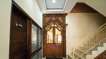 Um corredor com porta de madeira identificada como 'OFFICE', um arco de madeira decorativo e uma escada com corrimãos de madeira.
