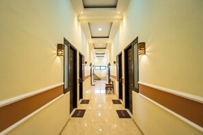 Pasillo de hotel con puertas a ambos lados, un mostrador de recepción al final y una escalera que sube a un piso superior.