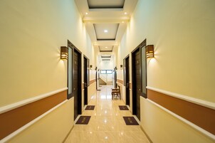 Pasillo de hotel con puertas a ambos lados, un mostrador de recepción al final y una escalera que sube a un piso superior.