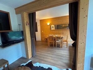 A room with a television, a dining area with wooden furniture, and a large mirror on the wall. - ❄️ LES ARCS 1800 ❄️ - Luxury Apartment – Les Arcs 1800 ⛷️ (Bourg-Saint-Maurice)
